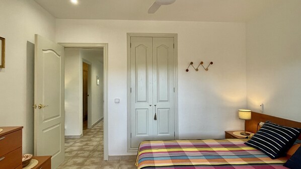 A bedroom with a bed, bedside table, lamp, and a door leading to another room.