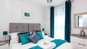 Ein Hotelzimmer mit Bett, Nachttisch, Kommode, Spiegel und einem Fenster mit Vorhängen.