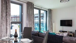 Ein modernes Hotelzimmer mit Essbereich, einer Sitzecke, einem Fernseher und einem Balkon mit Blick auf Gebäude.