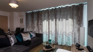 Ein modernes Wohnzimmer mit einem dunkelgrauen Sofa, einem Glastisch und einem Essbereich mit Tisch und Stühlen.
