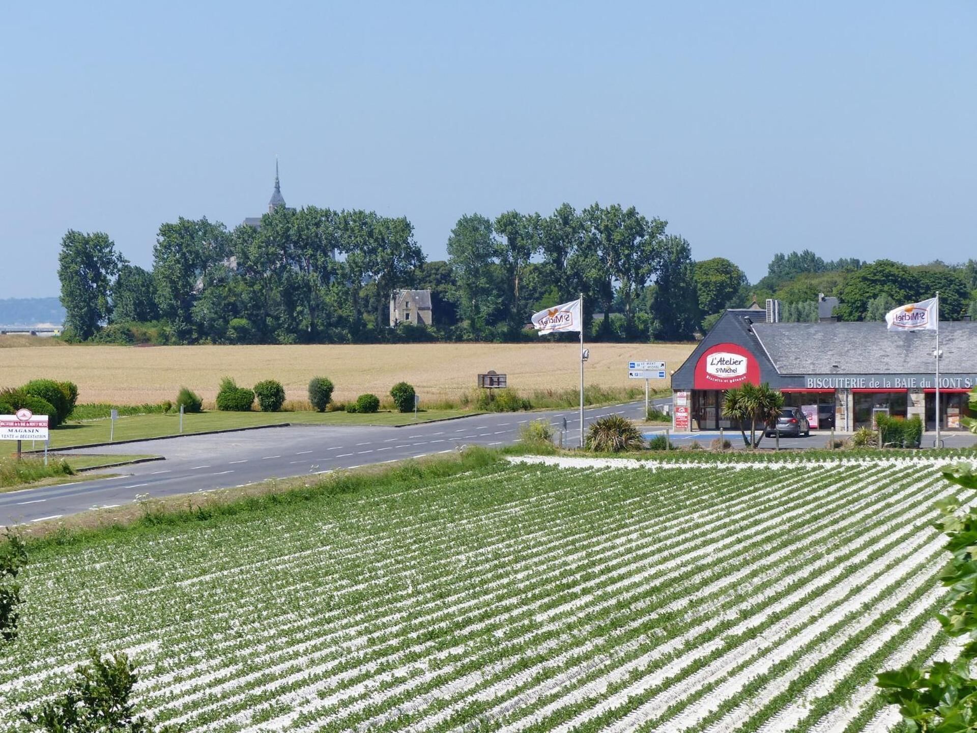 A rural landscape with a road, fields, a bakery, and a church in the background.