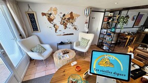 Un salon moderne avec une table basse ronde en bois, deux fauteuils blancs, une carte du monde accrochée au mur et une tablette affichant « Les vieilles digues » à l’écran.