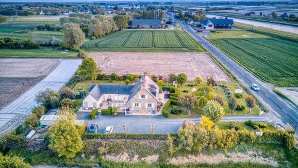 Vue aérienne d’un vaste domaine comprenant une maison principale, de vastes champs et une route.