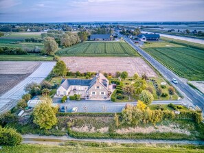 Eine Vogelperspektive auf einen weitläufigen Besitz mit einem Hauptgebäude, ausgedehnten Feldern und einer Straße.