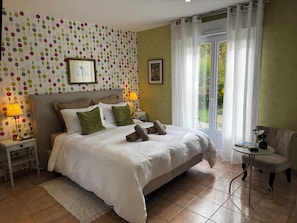 Ein Hotelzimmer mit einem Bett, zwei Nachttischen, einer Lampe, einem Sessel und Blick auf Grün durch das Fenster.