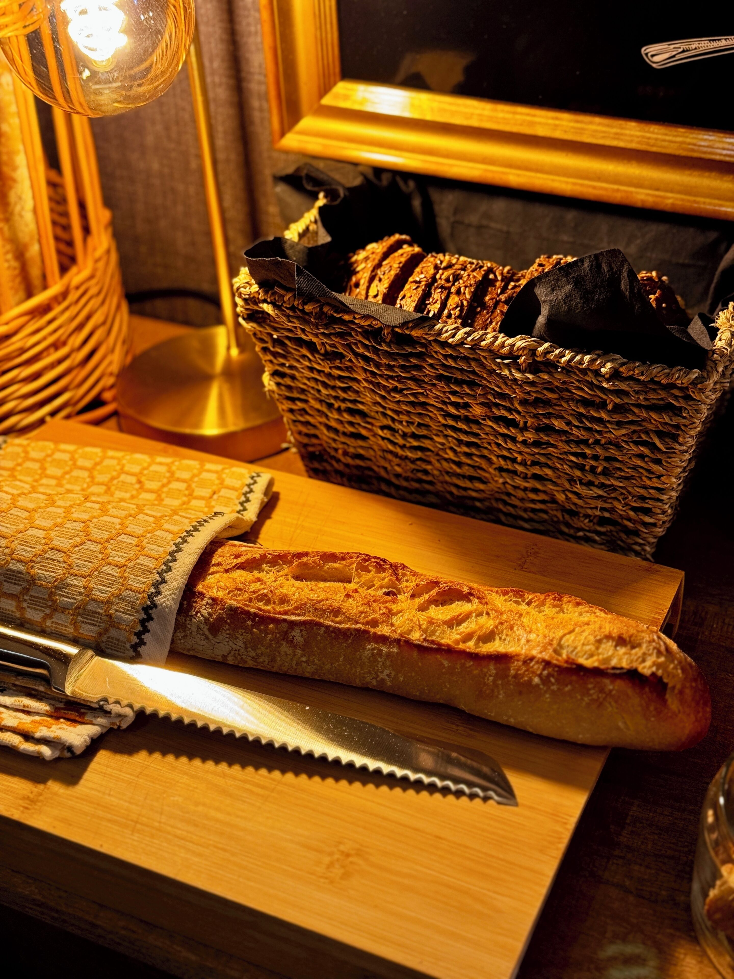 A wooden table with a basket of bread, a loaf of bread, and a knife.