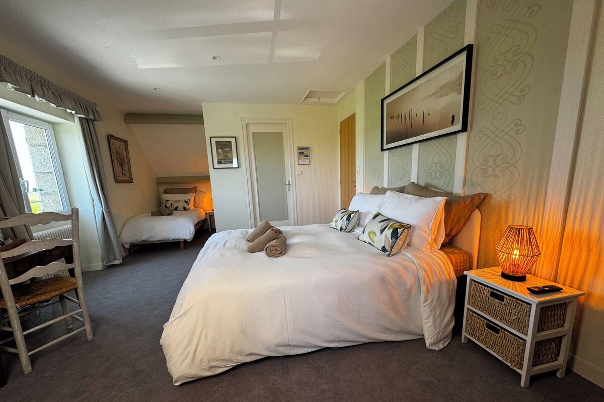Une chambre avec un grand lit, deux tables de chevet, une chaise et une fenêtre avec des rideaux.