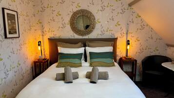 Una cama bien hecha con almohadas a rayas y un espejo redondo encima, frente a una pared con estampado de papel tapiz floral.