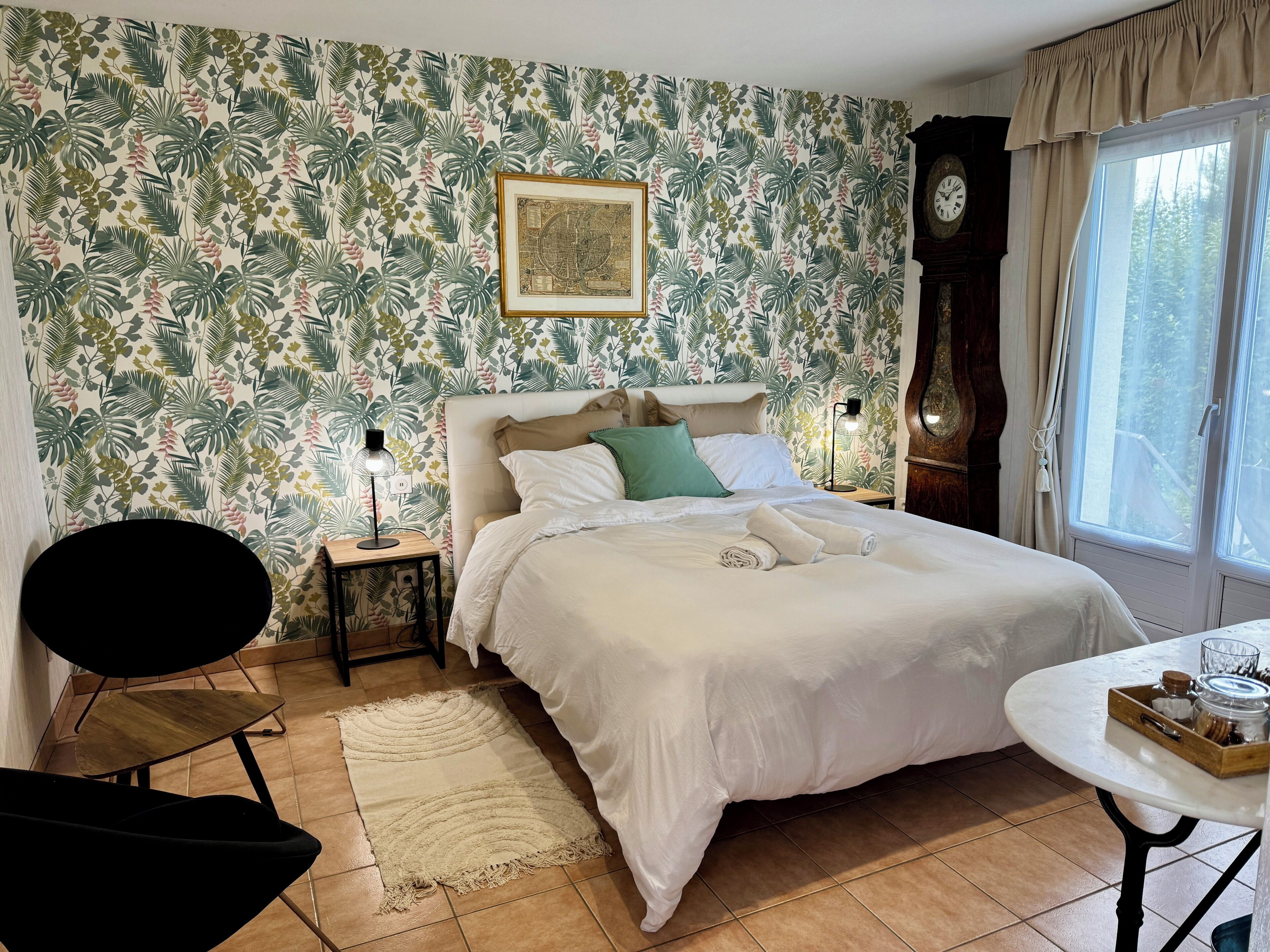 Une chambre à coucher avec un lit, une table de chevet, une horloge, une fenêtre et une petite table sur laquelle se trouve un plateau.