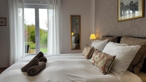 Une chambre d’hôtel avec un lit bien fait, une grande fenêtre avec des rideaux, un tableau encadré au mur et une lampe sur la table de chevet.