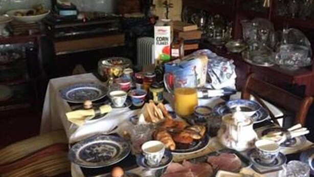 A dining table set with various dishes, glasses, and a coffee pot, surrounded by chairs and a cabinet with glassware. - Ms McCreadys Guest House (Doncaster)
