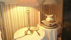 A room with striped wallpaper, a round table with a lamp, a decorative pitcher, and a small plate with a spoon. - Ms McCreadys Guest House (Doncaster)