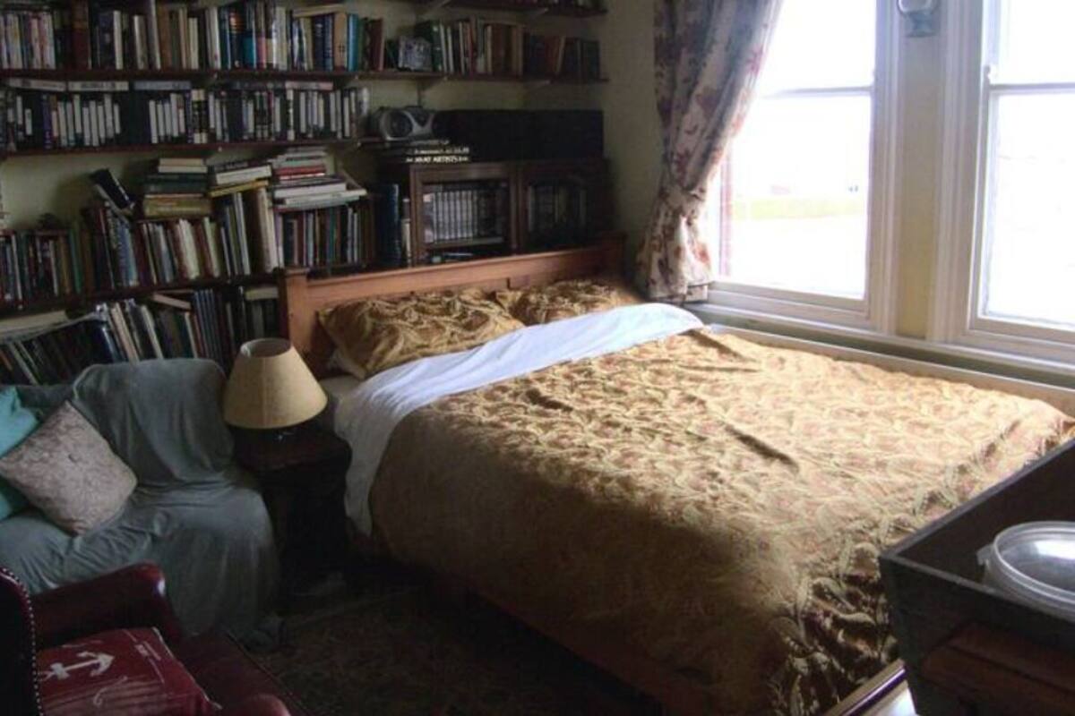 Um quarto com uma cama grande, uma estante cheia de livros, uma luminária e uma janela com cortinas.