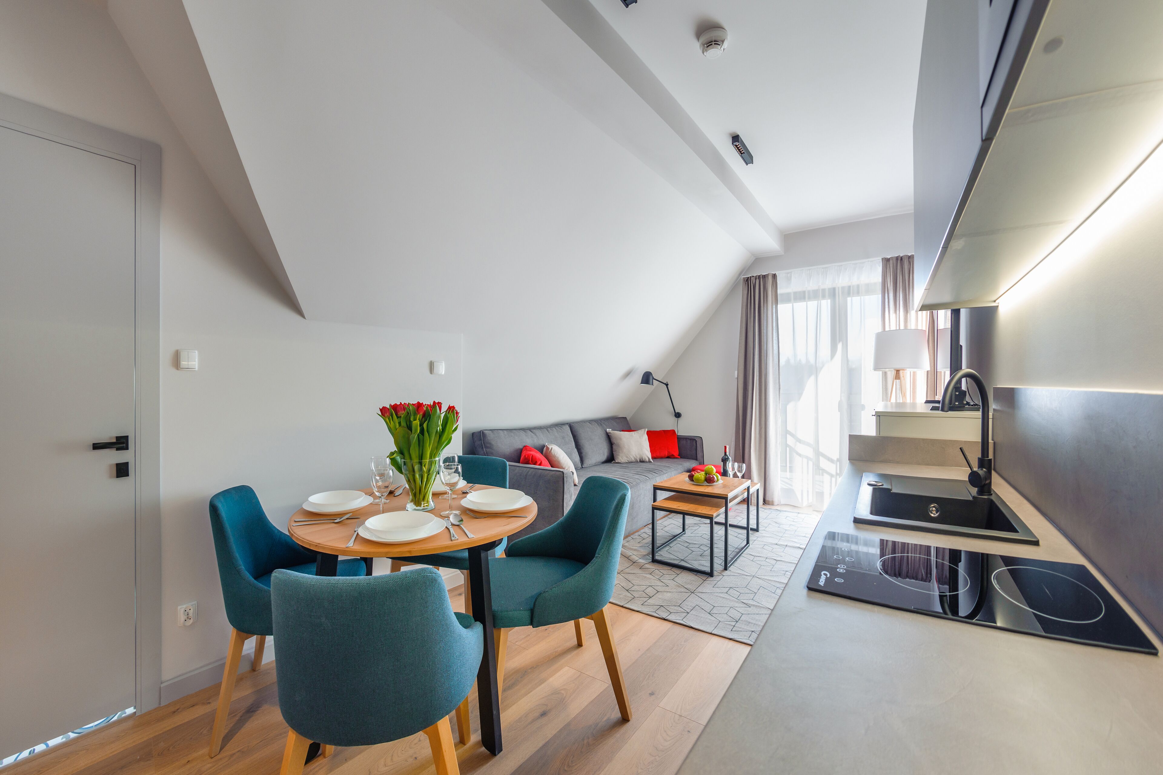 A modern kitchen with a built-in stove and a dining area with teal chairs and a wooden table.