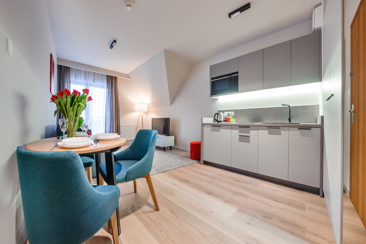 A modern kitchen with grey cabinets, a microwave, and a coffee machine. There is a dining area with teal chairs and a table set for two.