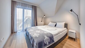 A modern bedroom with a large bed, a nightstand, a lamp, and a view of a balcony. - Sun & Snow Resorts A Białka Tatrzańska (Bukowina Tatrzanska)