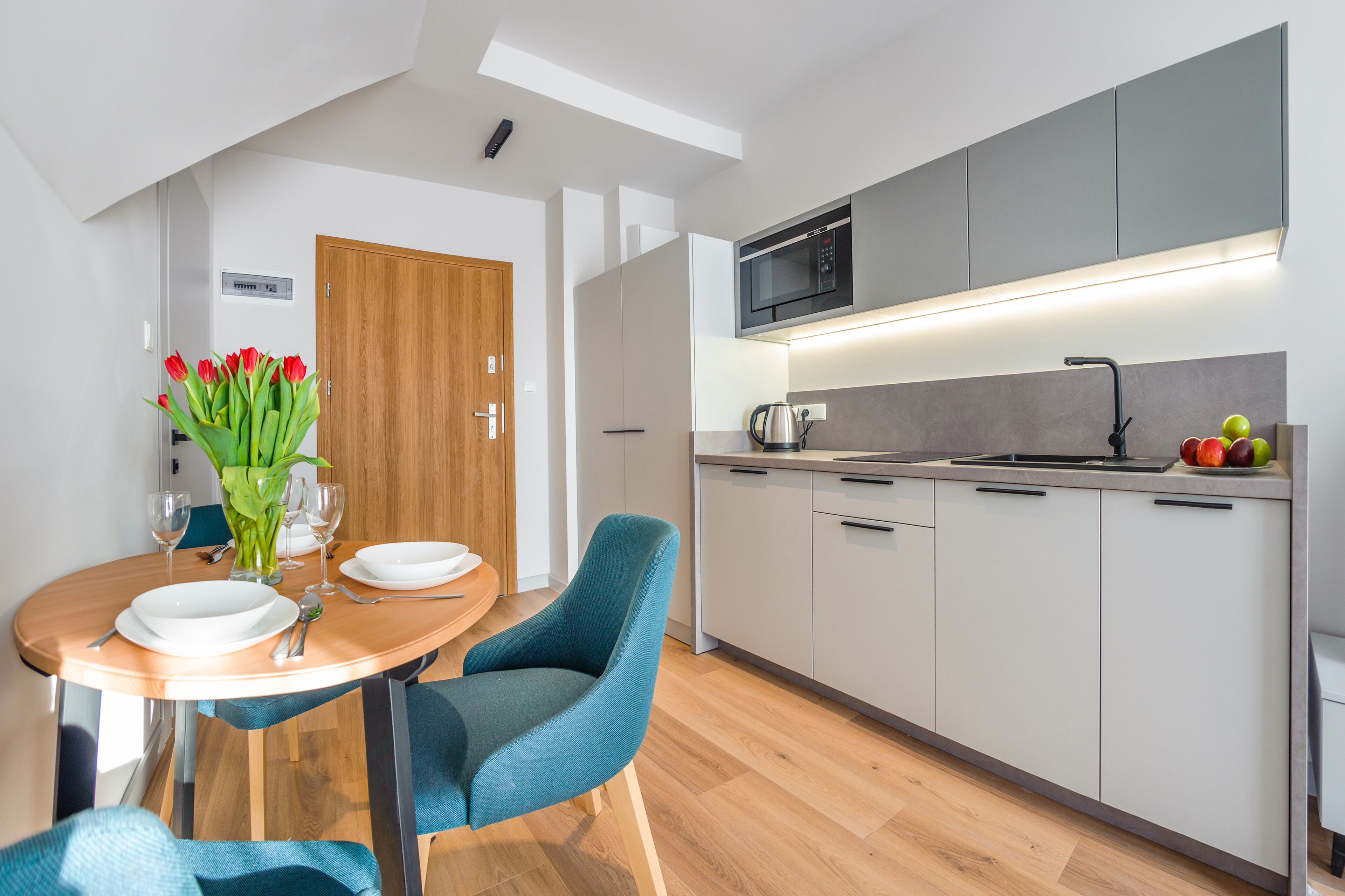 A modern kitchen with grey cabinets, a microwave, and a sink. There is a dining table with chairs and a vase of red tulips.