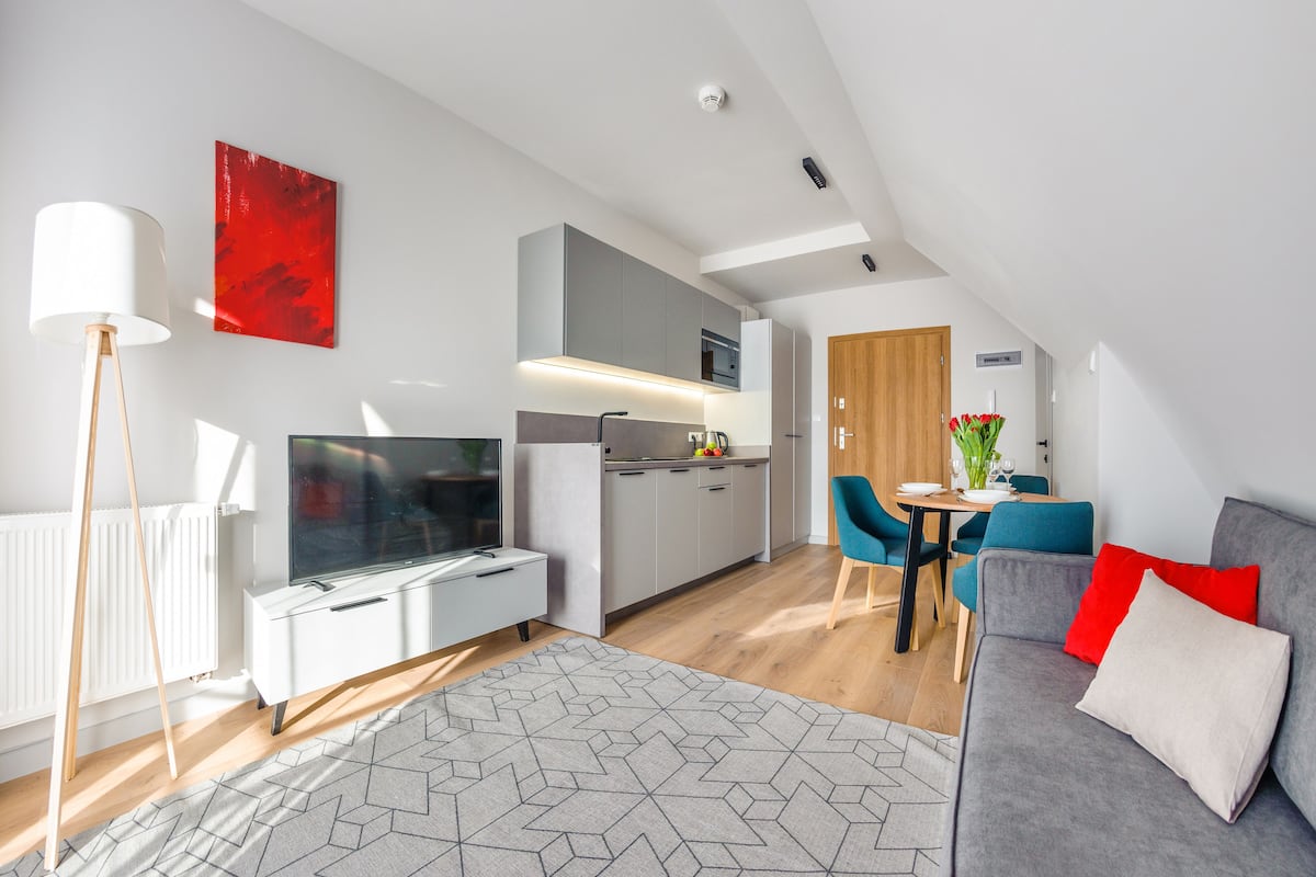 A modern living room with a grey sofa, a TV, and a dining area with a table and chairs.