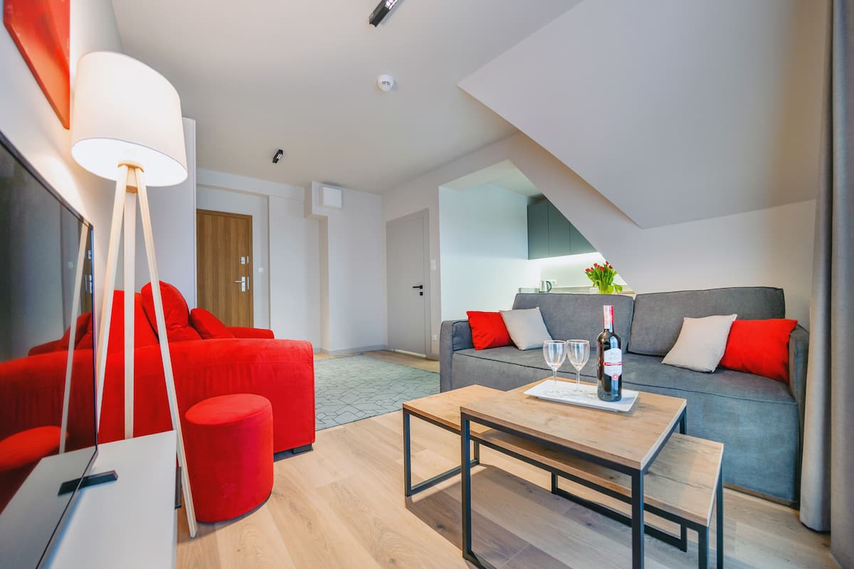 A modern living room with a red sofa, a grey sofa, a wooden coffee table, and a red ottoman.