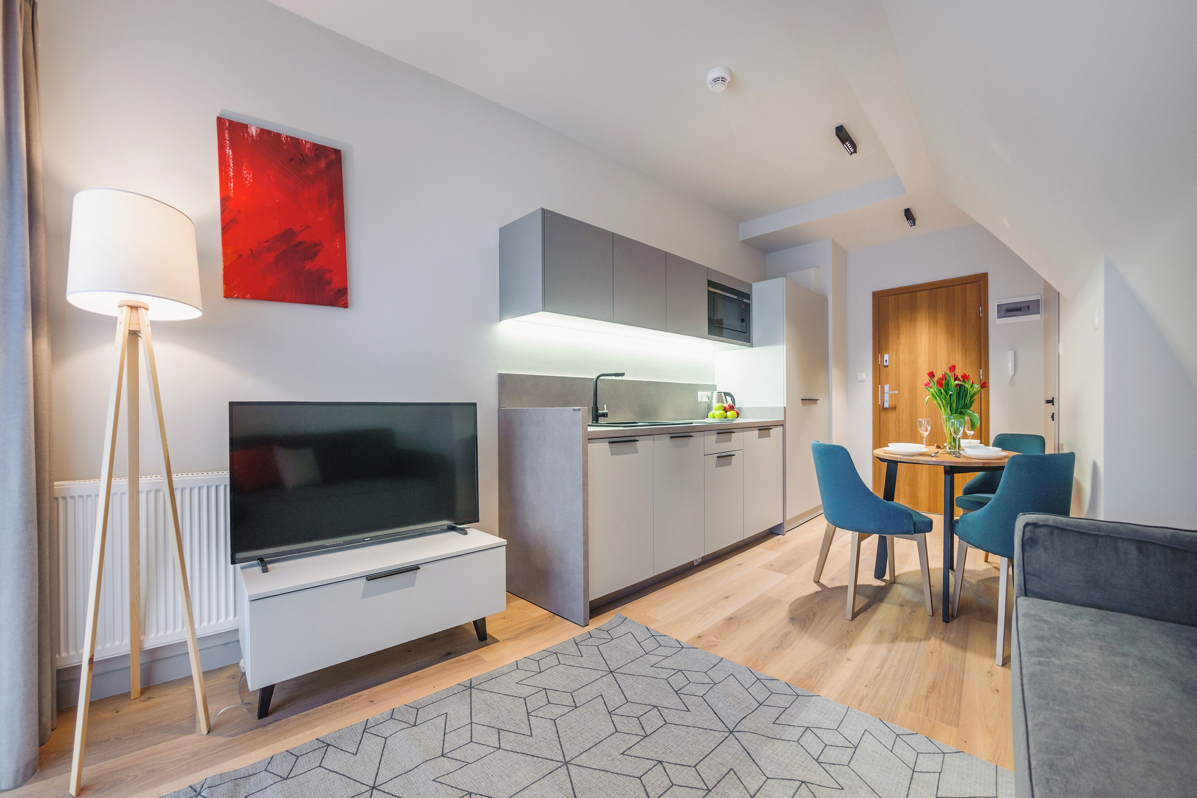 A modern kitchen with a flat-screen TV, a dining area with blue chairs, and a red abstract painting on the wall.