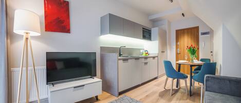A modern kitchen with a flat-screen TV, a dining area with blue chairs, and a red abstract painting on the wall.