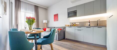 A modern kitchen with grey cabinets, a microwave, and a dining area with teal chairs and a wooden table.