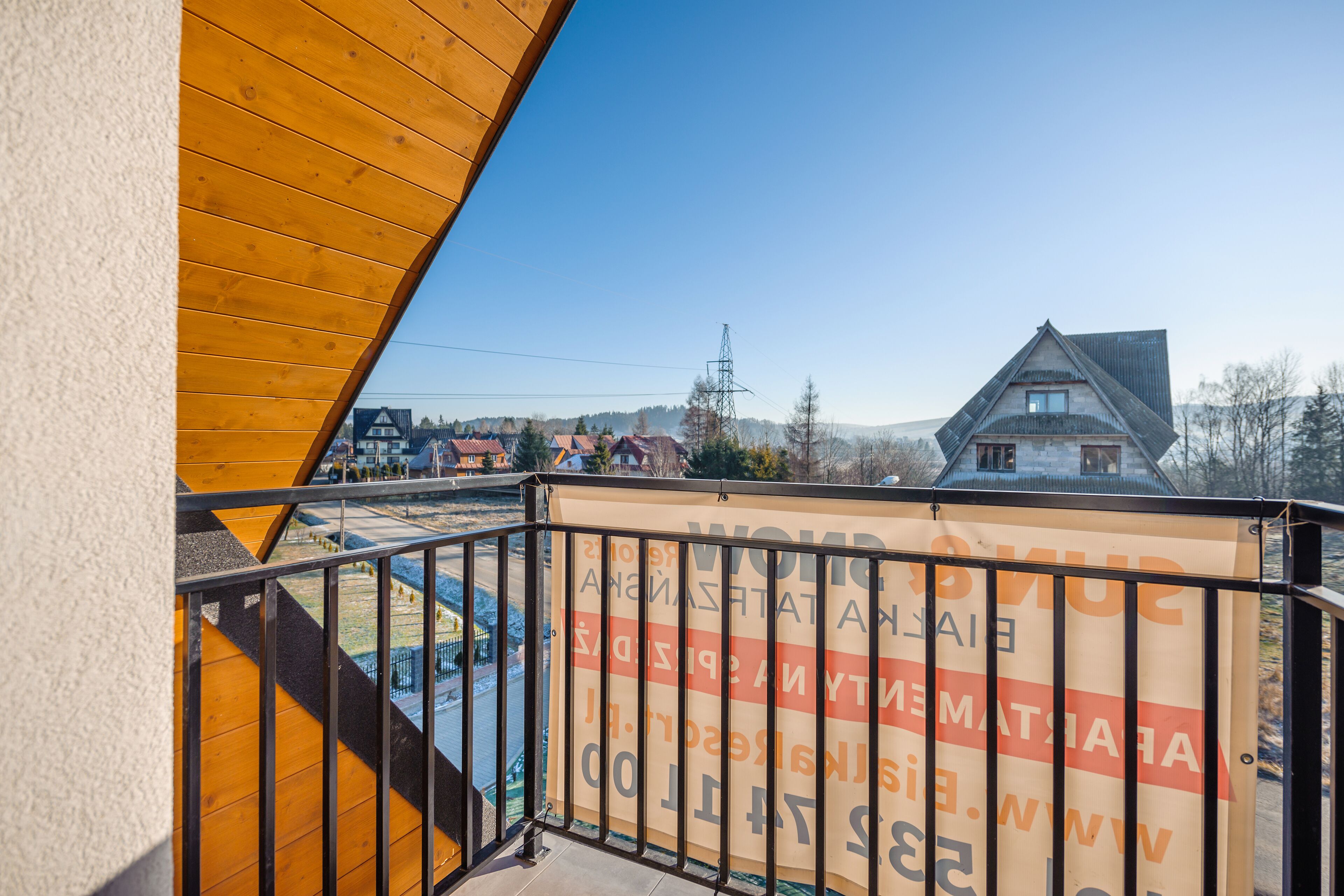 A balcony with a view of a village, a wooden structure, and a banner with text.