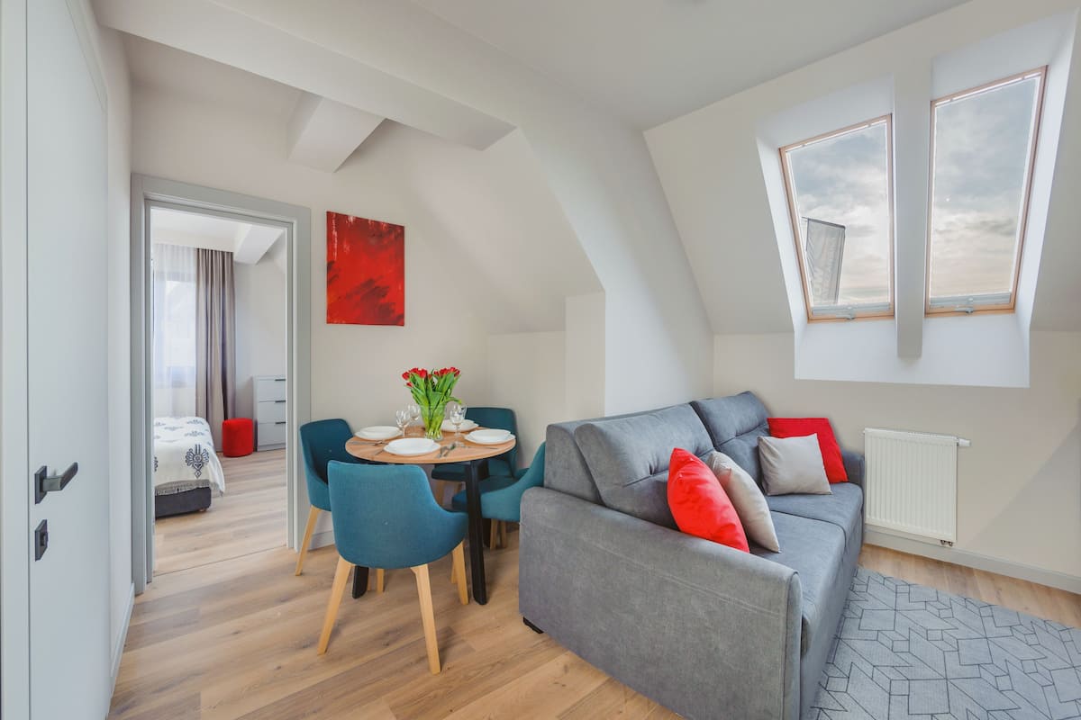 A modern living room with a grey sofa, red cushions, a dining table with chairs, and a red abstract painting.