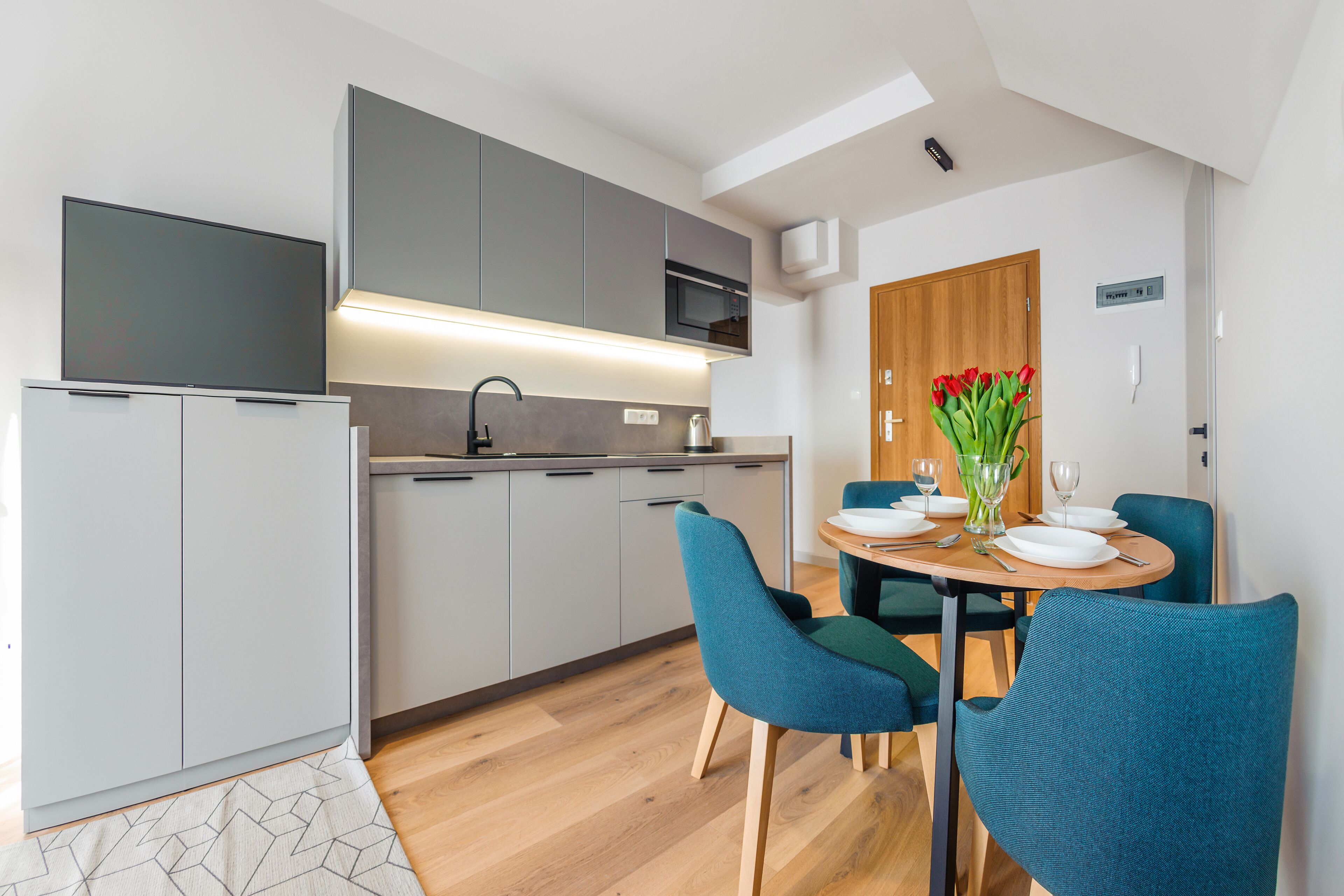 Una cocina moderna con armarios grises, un microondas integrado y una mesa de comedor de madera con sillas color turquesa.