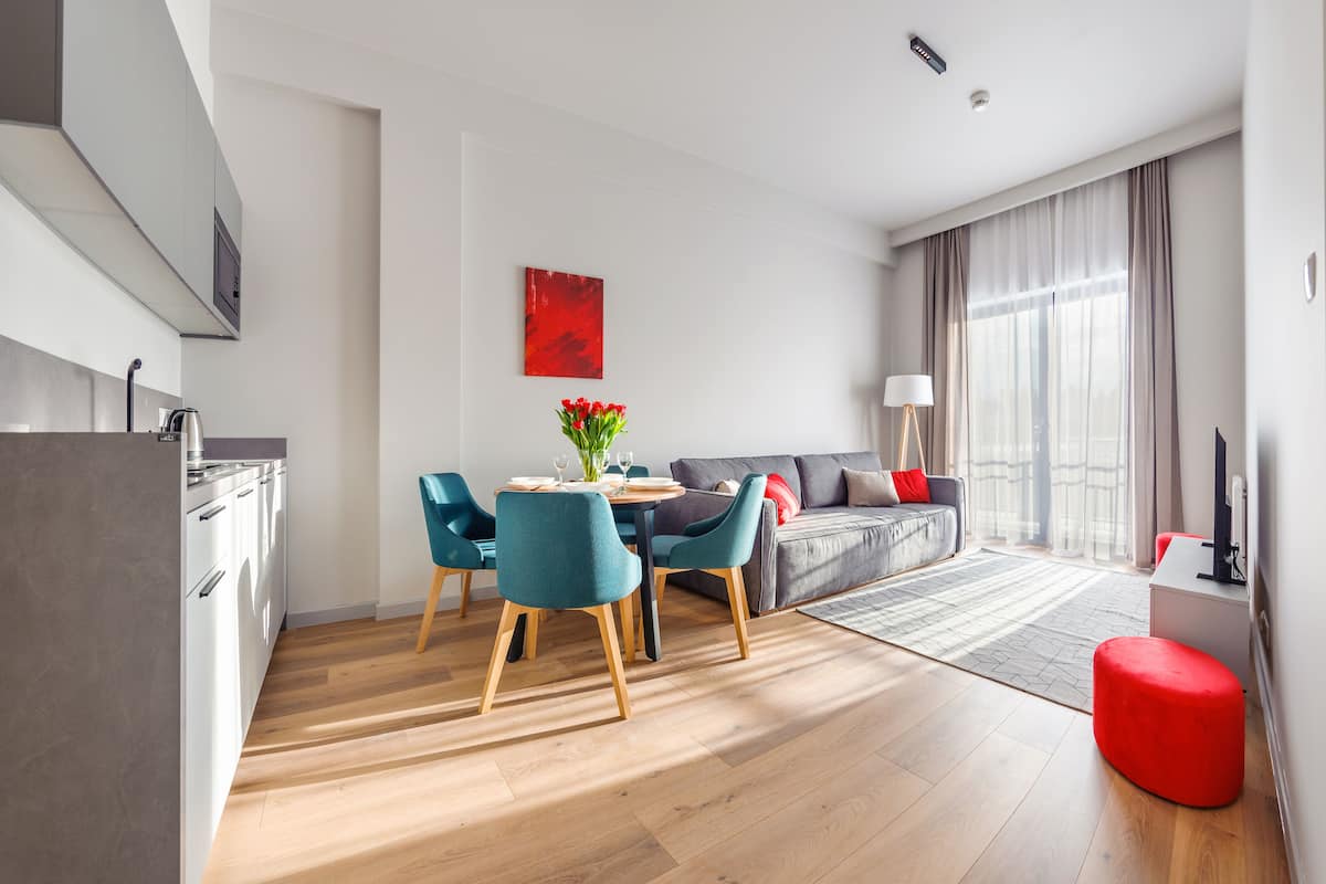 A modern living room with a dining area, a sofa, and a red ottoman.