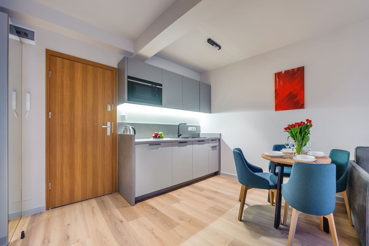 A modern kitchen with grey cabinets, a wooden door, and a dining area with teal chairs and a table set for two.