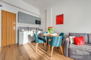 A modern kitchen with grey cabinets and a microwave, a dining area with teal chairs and a table, and a grey sofa with a red pillow. - Sun & Snow Resorts A Białka Tatrzańska (Bukowina Tatrzanska)