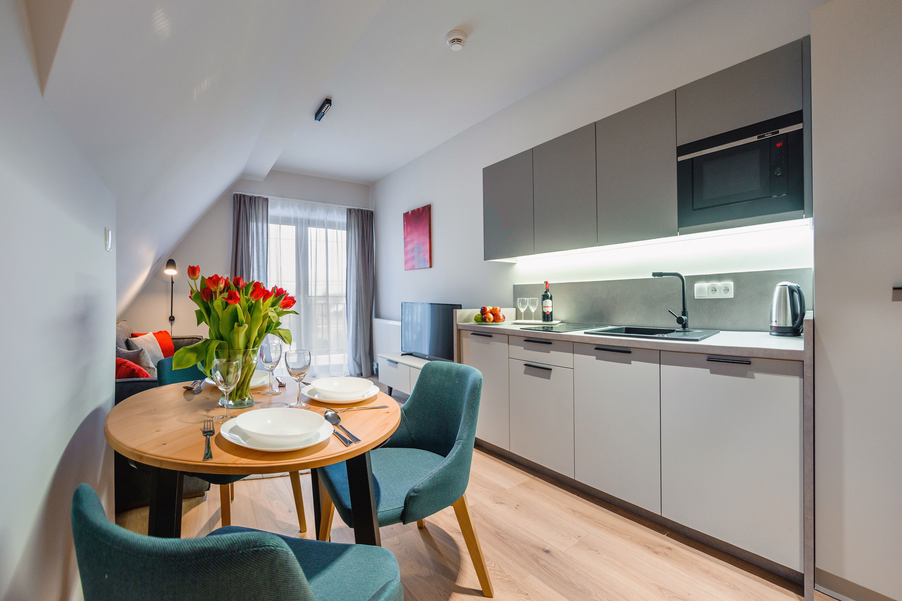 A modern kitchen with a dining area, equipped with a microwave, sink, and kettle.