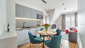A modern kitchen with grey cabinets, a microwave, and a sink. There is a dining area with teal chairs and a round table set for four. A bottle of wine and glasses are on the counter. - Sun & Snow Resorts A Białka Tatrzańska (Bukowina Tatrzanska)