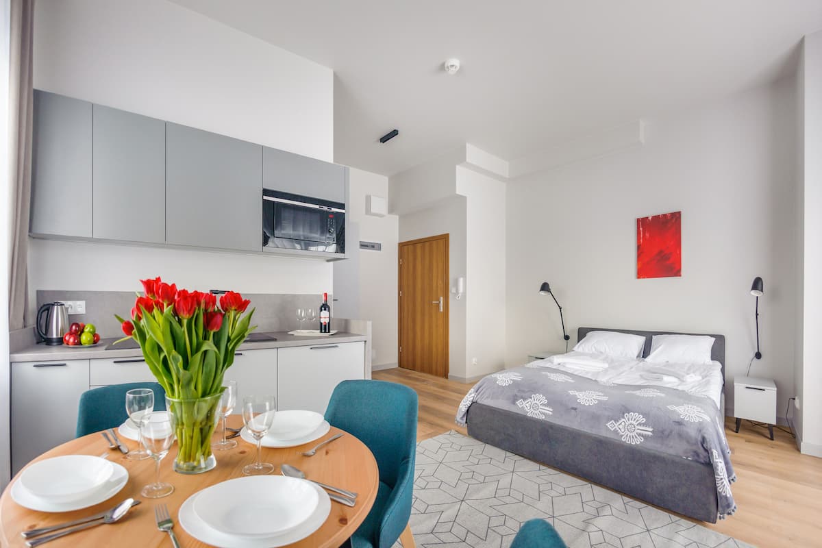 A modern hotel room with a dining area, a bed with a patterned bedspread, and a red artwork on the wall.