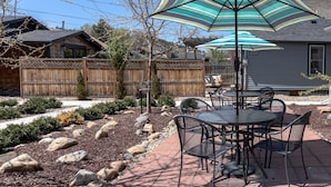 An outdoor patio with a round table and chairs, surrounded by a wooden fence and a landscaped garden. - Downtown 1 Bedroom Charmer - Walk, Bike, Visit, Enjoy!! (Rapid City)