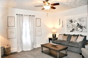 A living room with a ceiling fan, a sofa, a coffee table, and framed artwork on the walls.