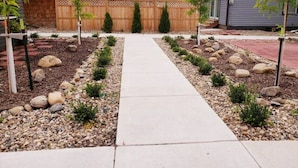 A residential backyard with a concrete pathway, small shrubs, and a wooden fence. - Downtown 1 Bedroom Charmer - Walk, Bike, Visit, Enjoy!! (Rapid City)