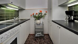 A modern kitchen with white cabinets, a stainless steel sink, a coffee maker, and a vase with flowers. - Hotel Blanco (Hamburg)