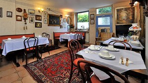A dining area with tables set for two, a patterned rug, and a view of the outdoors through a window. - Hotel Blanco (Hamburg)