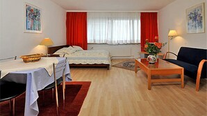 A room with a bed, a table, a sofa, and a window with red curtains. - Hotel Blanco (Hamburg)