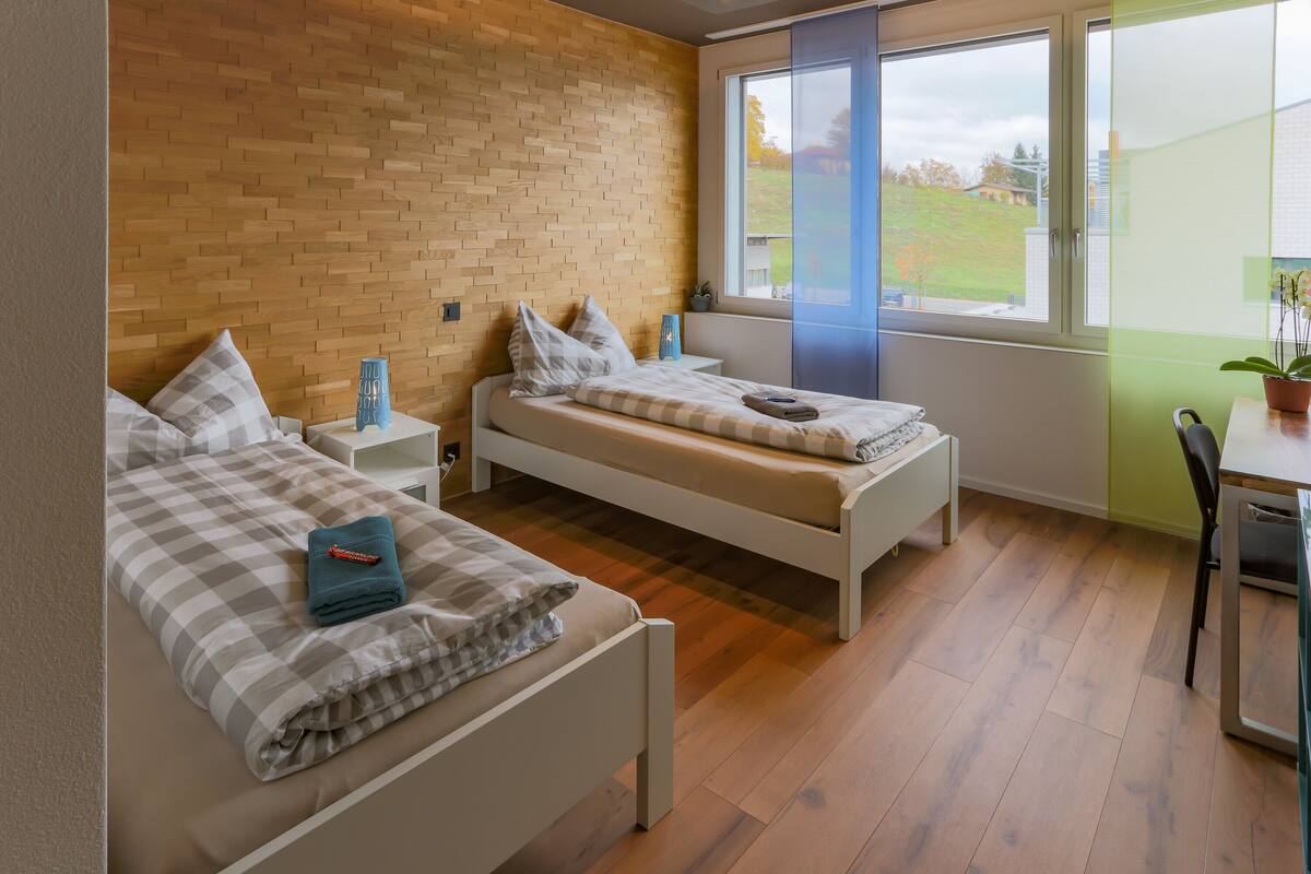 A bedroom with two beds, a window, and a view of the outside.