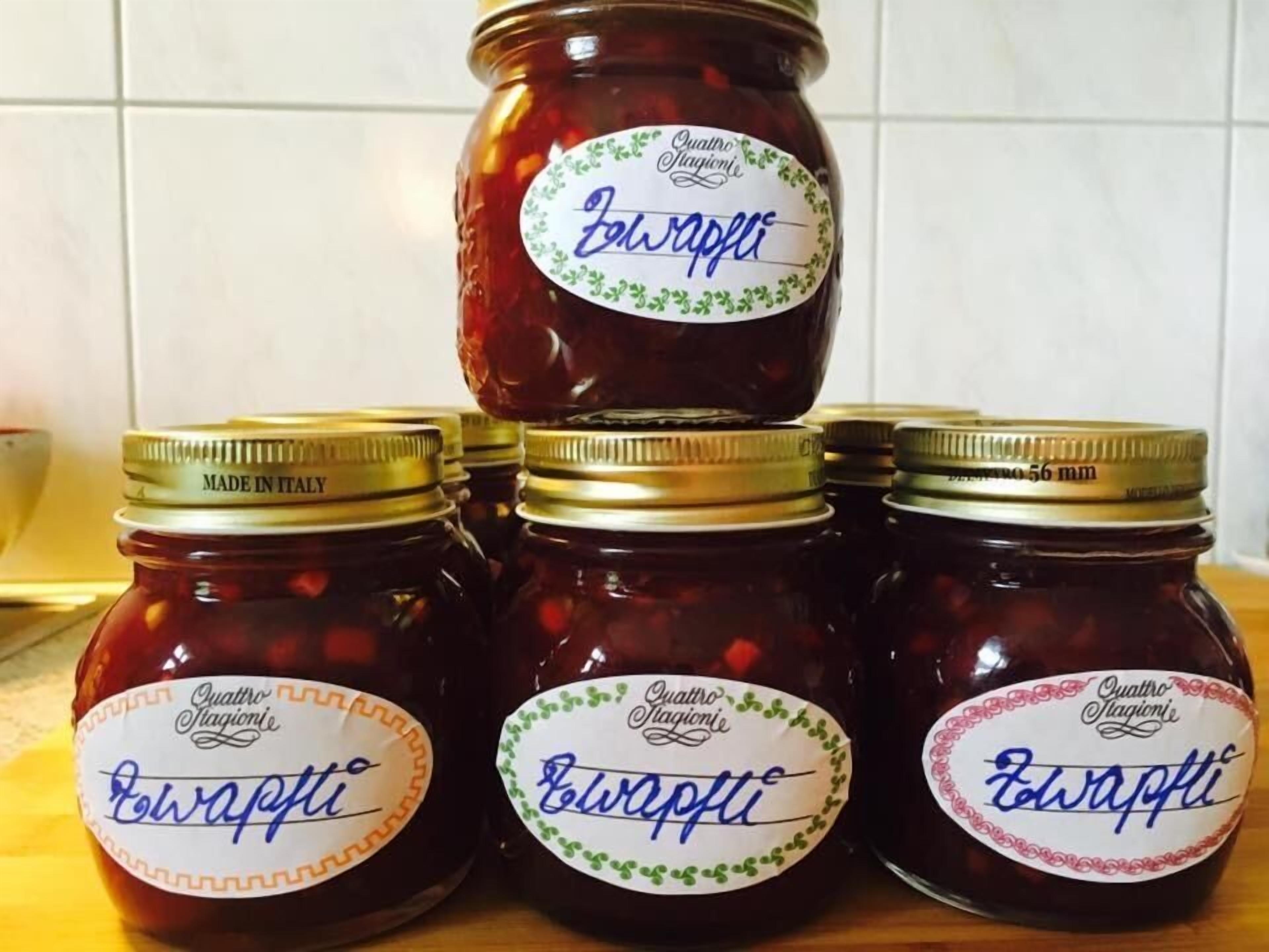 Four jars of 'Zavapfi' jam with gold lids and labels, arranged on a wooden surface.