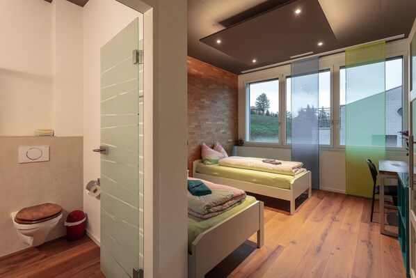 Un dormitorio moderno con dos camas, piso de madera, pared de ladrillo decorativa y un ventanal grande.