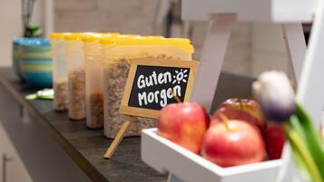 Una barra de desayuno con un cartel que dice 'Guten Morgen', un recipiente con granola y un bol de manzanas.