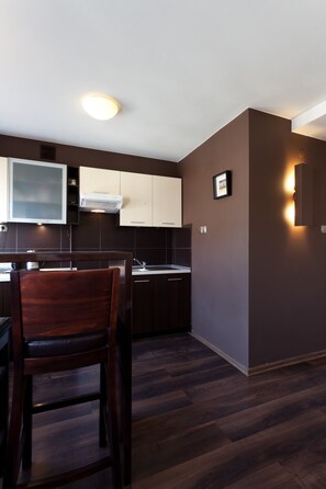 A modern kitchen with dark wood flooring, white and dark brown cabinets, and a built-in microwave.