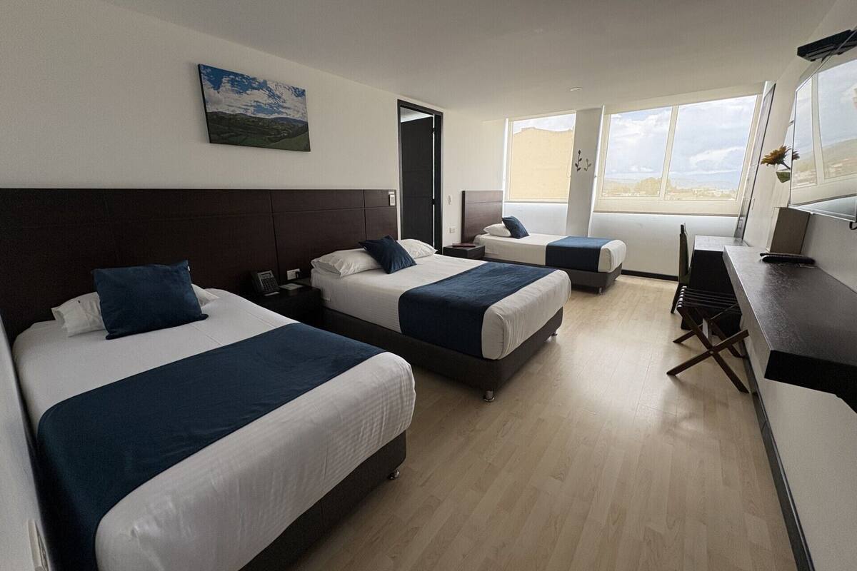 A hotel room with two beds, a desk, and a window with a view.