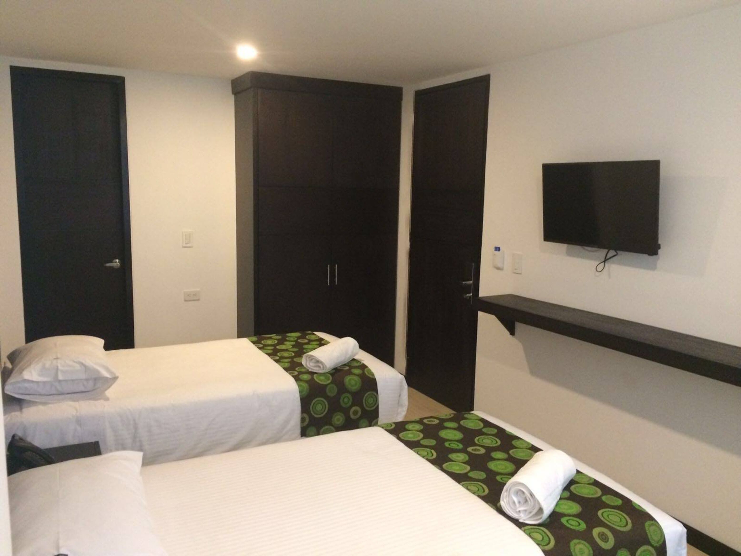 Una habitación de hotel con dos camas individuales, un televisor montado en la pared y un armario.