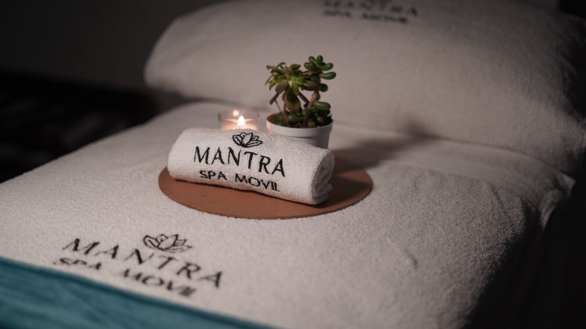 Una camilla de spa con una toalla que dice "MANTRA SPA MOVIL" y una pequeña planta en maceta.