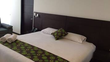 A neatly made bed with a patterned bedspread, pillows, and rolled towels on a dark headboard.